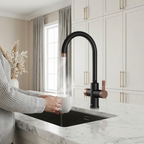 Person washing a white mug under a modern black and copper kitchen faucet in a bright kitchen.